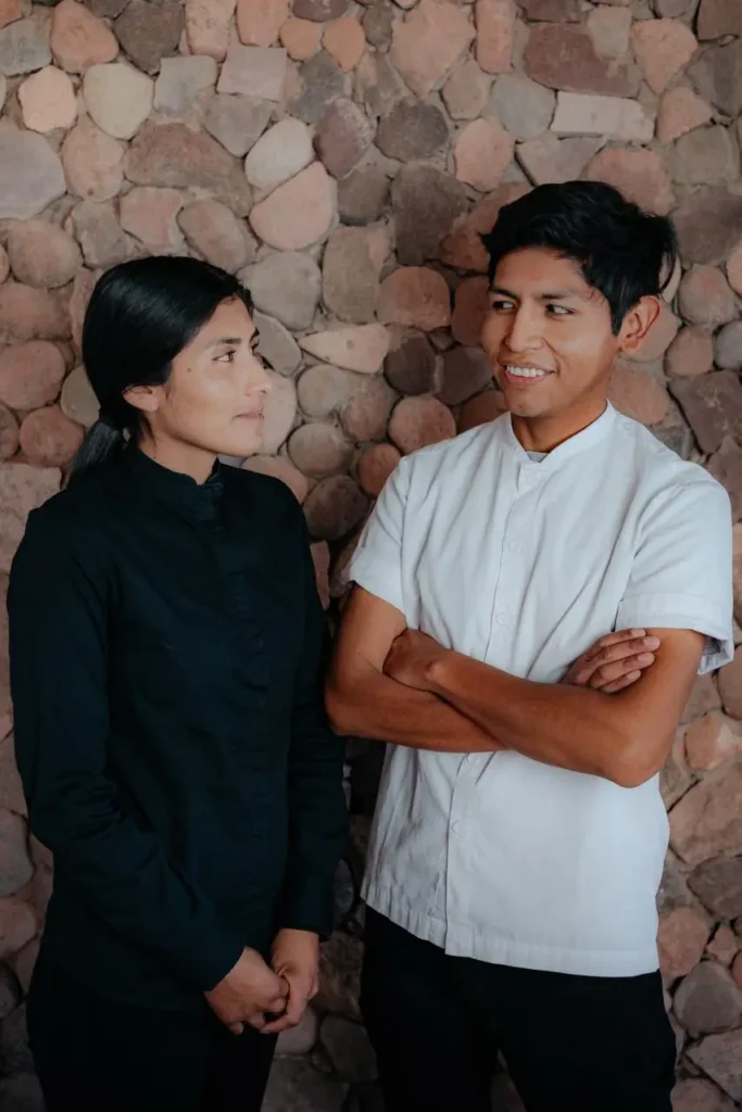 Chef Sergio Armella y Carolina Colque posan frente a muro de piedra en San Pedro de Atacama